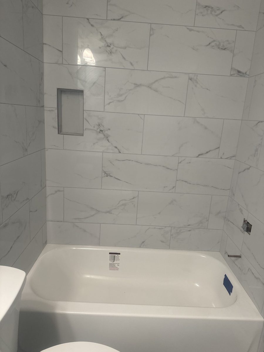 An alcove bathtub with a full-height marble-look tile surround