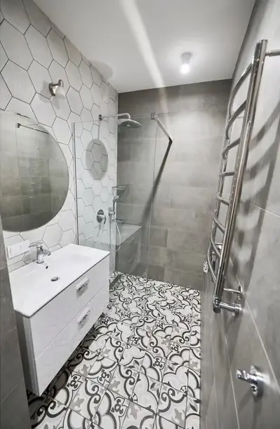 Compact finished bathroom with a patterned tile floor, round mirror and a heated towel rail