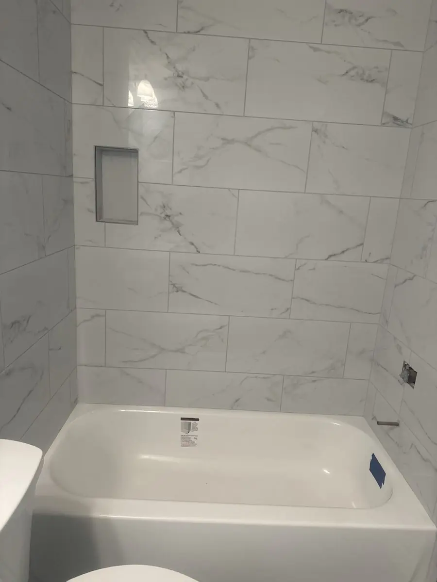 Alcove bathtub with a full-height marble-look tile surround and a recessed shelf niche
