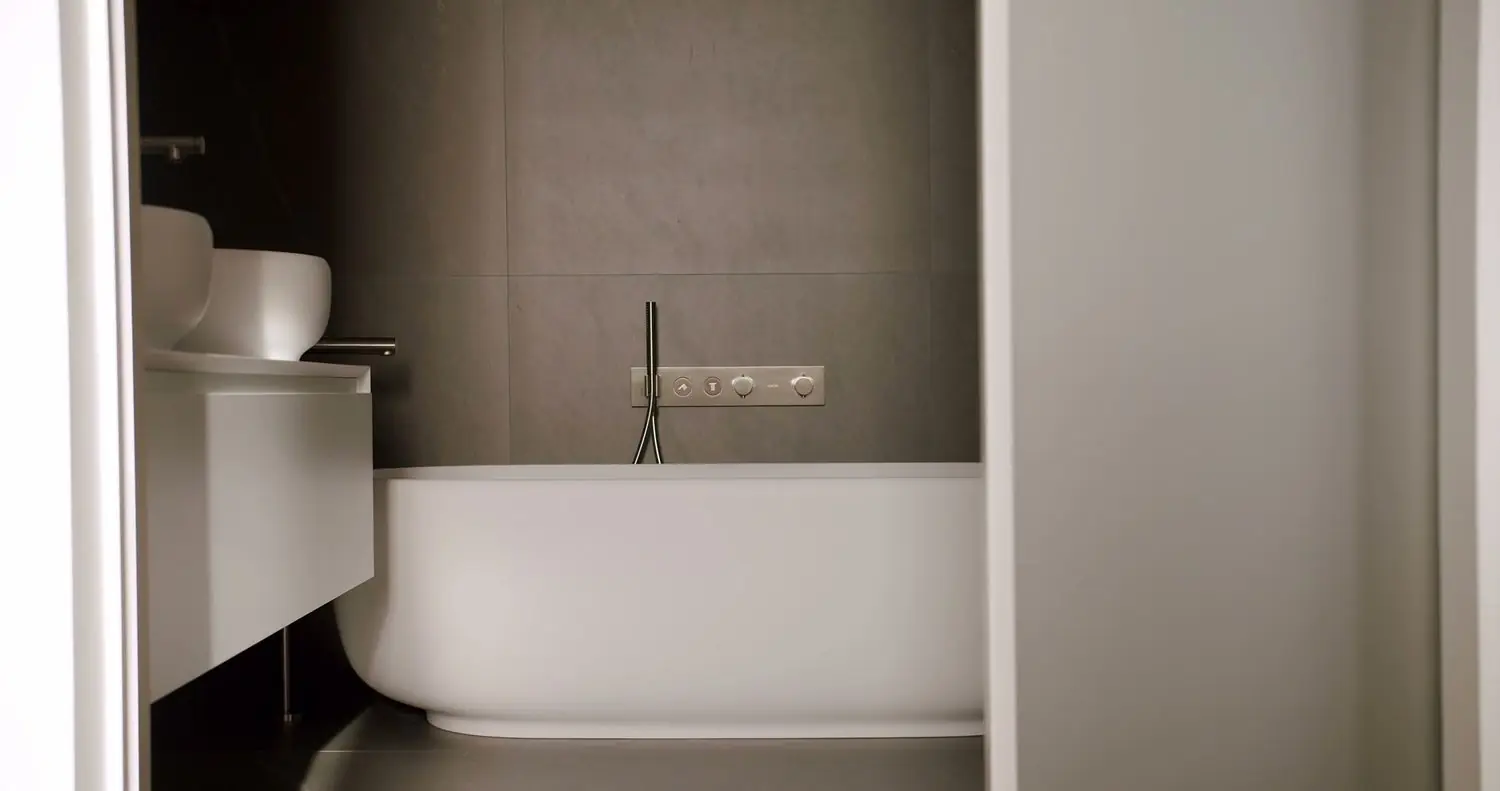 Alcove bathtub with a wall-mounted filler and full-height stone tile surround