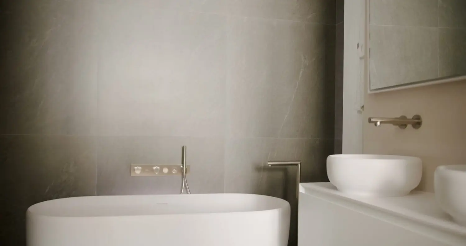 A freestanding bathtub beside a vessel basin with a brass filler