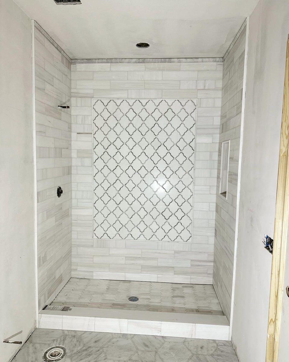 A white tiled shower with a tall arabesque mosaic feature panel