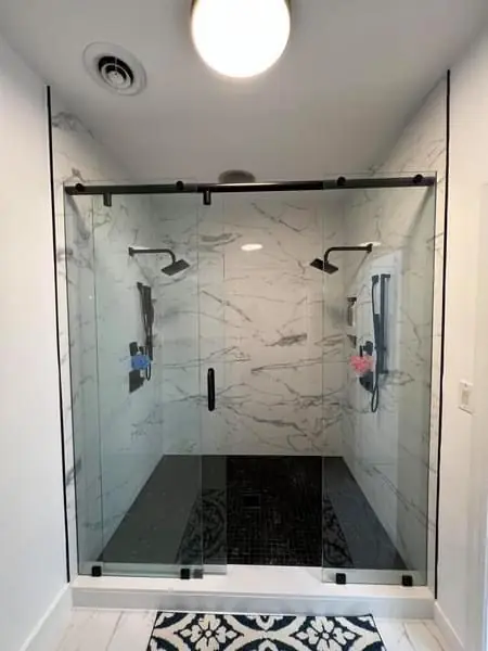 Marble-tiled walk-in shower with a black sliding door and a patterned tile floor