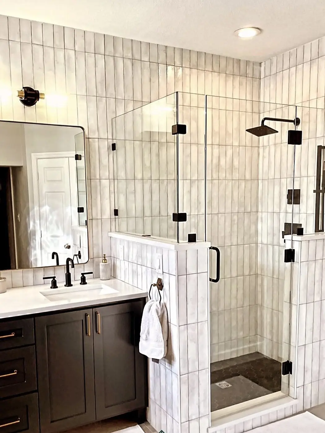A walk-in shower with stacked vertical tile and matte black fixtures