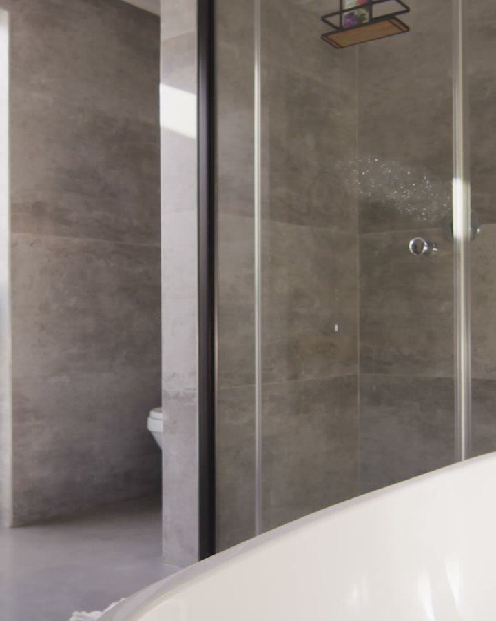 Stone-tiled shower with a flush entry and a clear glass panel beside a freestanding tub