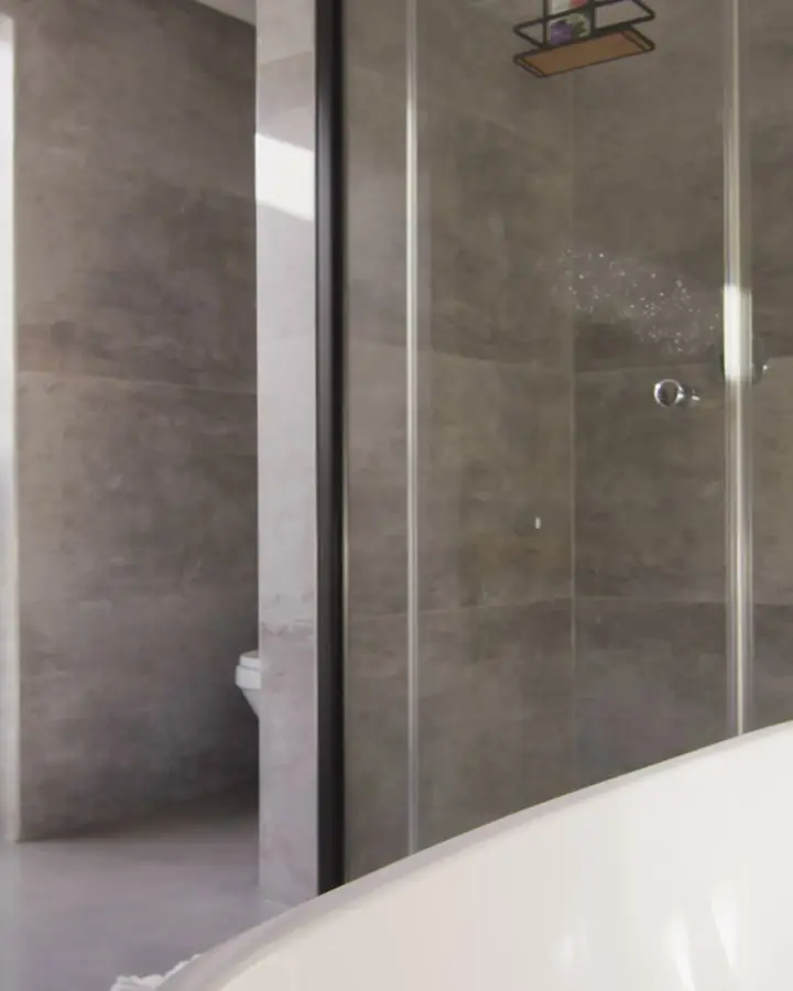 Stone-tiled shower with a flush entry and a clear glass panel beside a freestanding tub