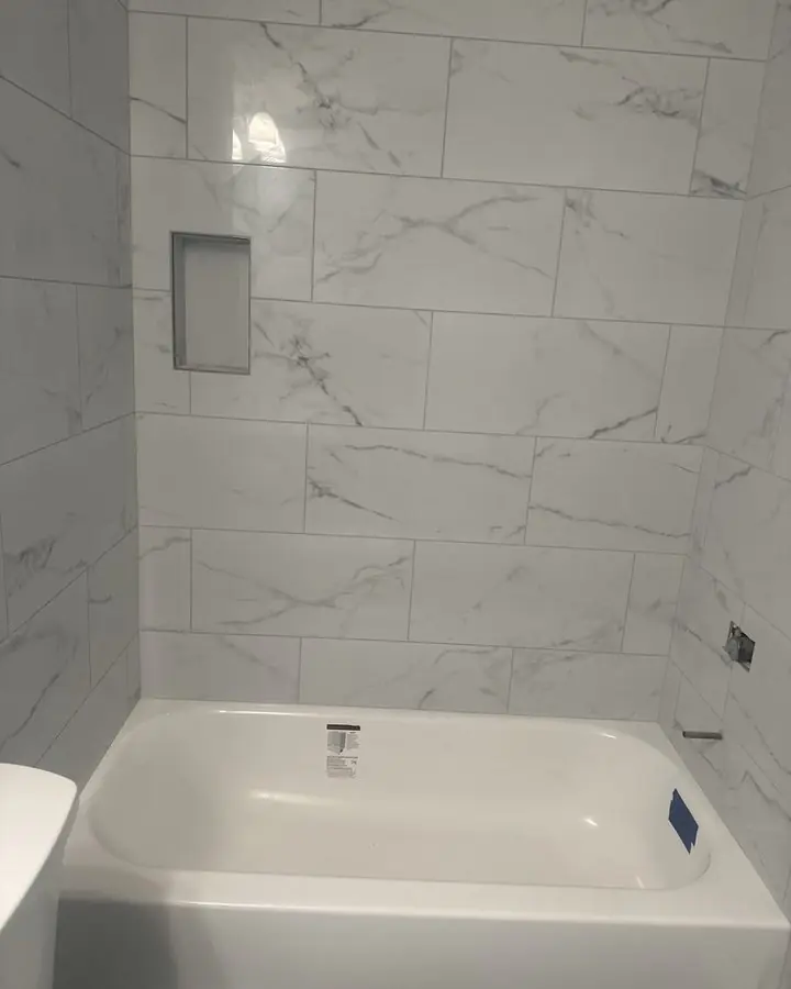 Alcove bathtub with a full-height marble-look tile surround and a recessed shelf niche