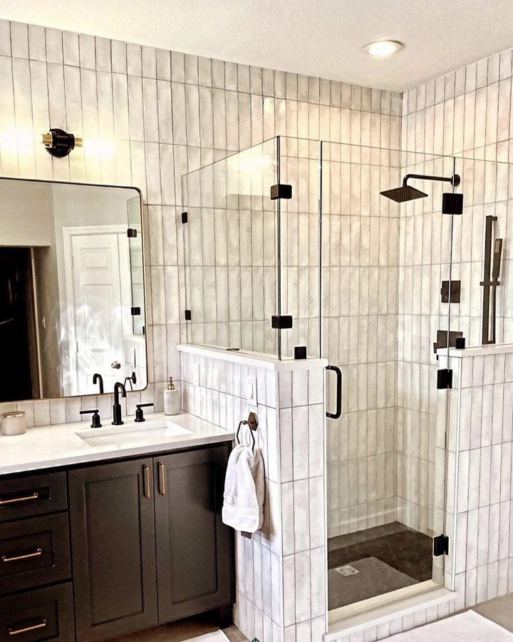 Frameless glass shower enclosure against white vertical wall tile with matte black fixtures