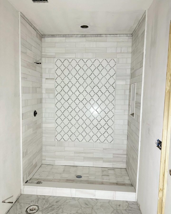 White tiled shower with a tall arabesque mosaic feature panel set into the back wall