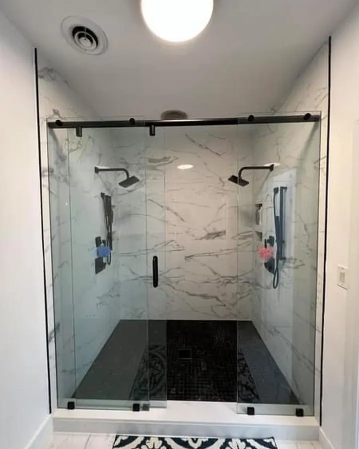 Marble-tiled walk-in shower with twin shower heads and a black frameless sliding door
