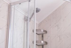 Shower enclosure corner where the fixed panel meets tile, sealed with silicone at the change of plane