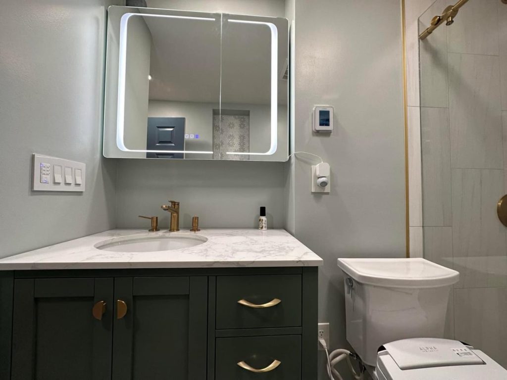 Renovated bathroom with a green vanity, brass tapware and a backlit mirror cabinet