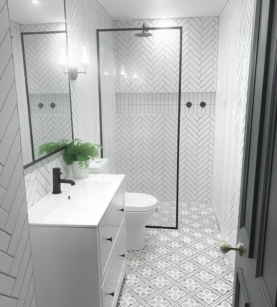 Narrow renovated bathroom with a herringbone-tiled walk-in shower, glass panel and a patterned tile floor